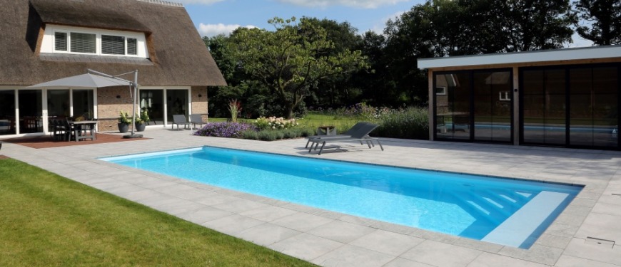 Ervaar ongekende luxe met een zwembad van Aqua Optimaal Een langwerpig buitenwembad met ligstoelen en een terras bij een rietgedekte villa.