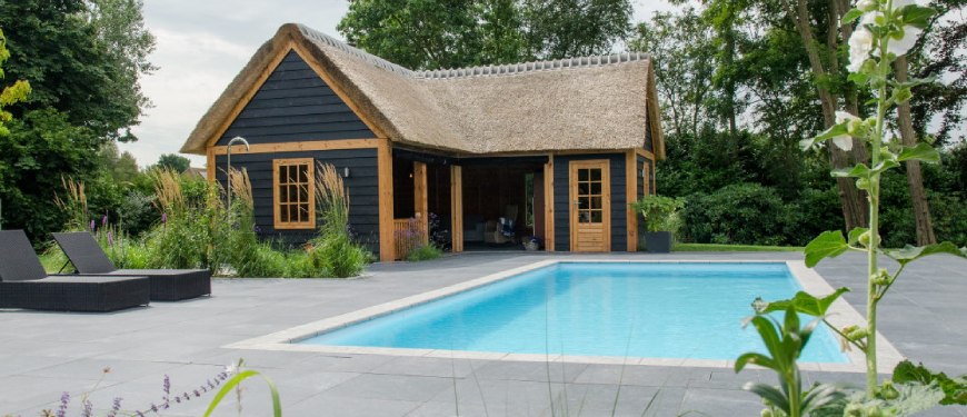 Zwembad laten plaatsen in Zuidwolde? Zwarte houten poolhouse met rieten dak naast een buitenzwembad.