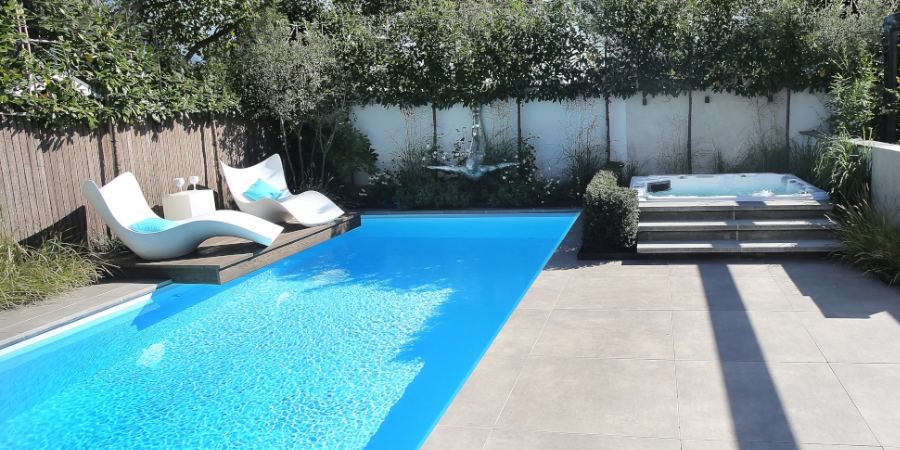  Buitenzwembad met helderblauw water omgeven door een tuin met een jacuzzi en moderne lounge stoelen